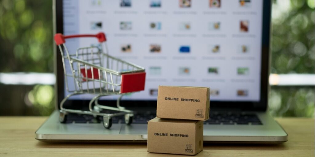 Miniature cardboard boxes with shopping cart and laptop computer background. Concept of online shopping